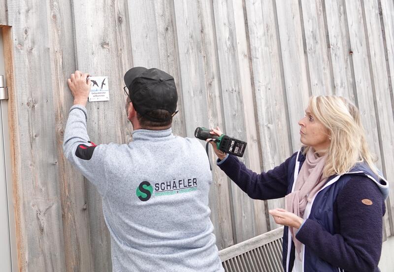 Bild vergrößern: Herr und Frau Schäfler installieren die Plakette »Gebäudebrüter Willkommen« an ihrer Gewerbehalle in Weißensberg.